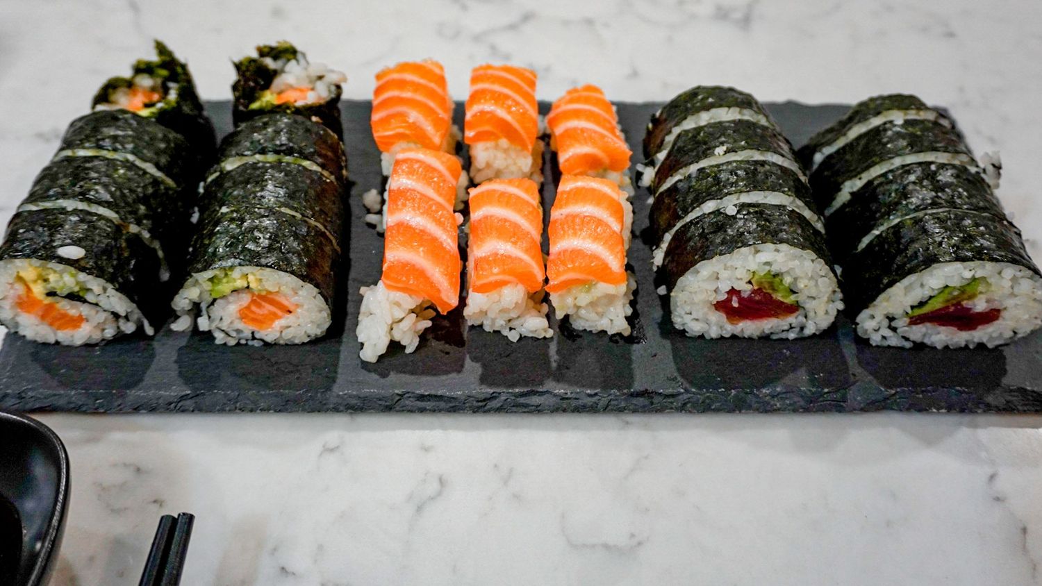 Fresh salmon and maki sushi rolls displayed in an organized line on a light surface.