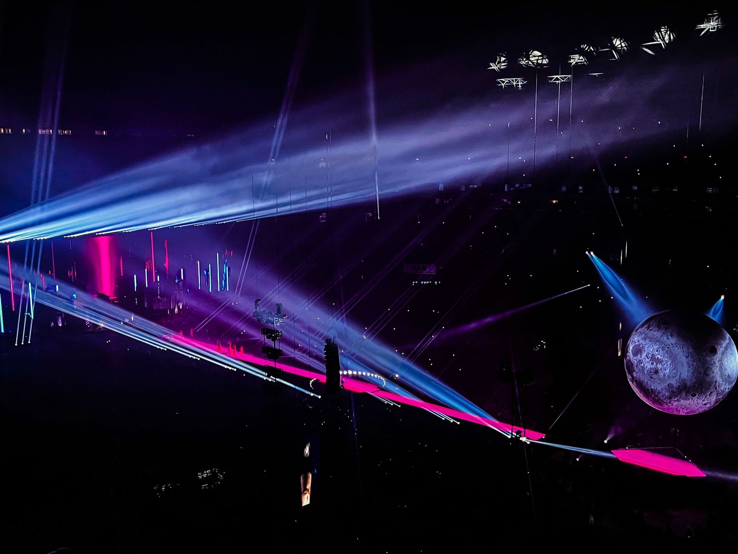 Concert stage with dramatic blue and pink lighting effects and spotlights in dark venue.