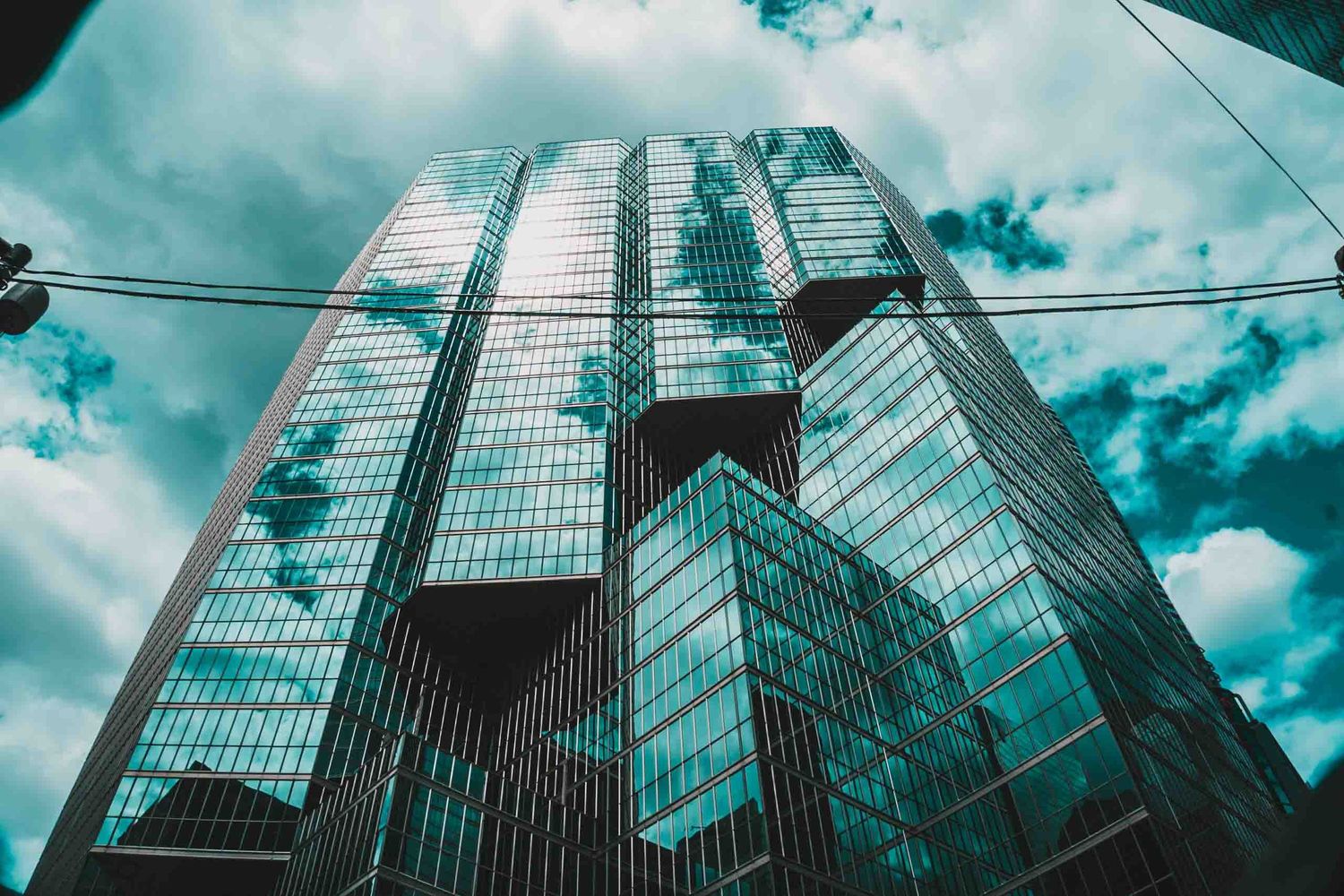 Glass skyscrapers photographed from below against turquoise sky with dramatic clouds.