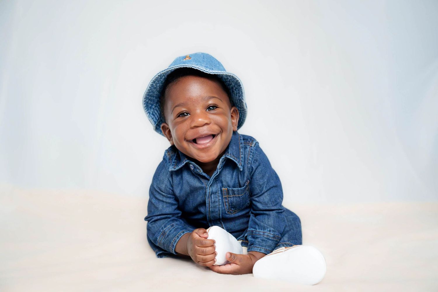 Child wearing denim jacket and hat lying down with cheerful expression.