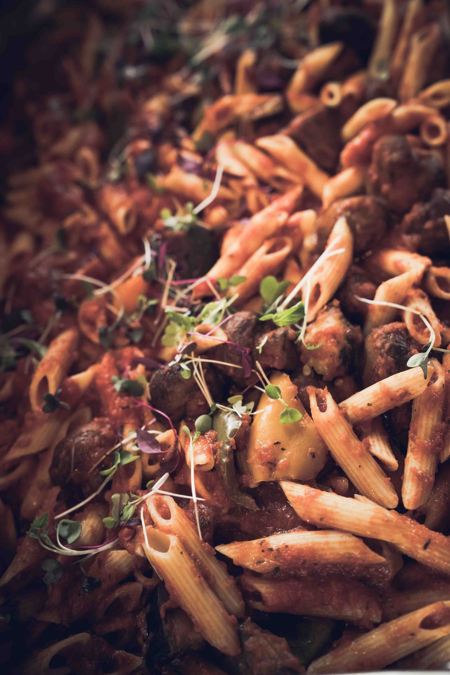 Penne pasta with meatballs in tomato sauce, garnished with fresh microgreens, served as a hearty Italian-inspired dish.