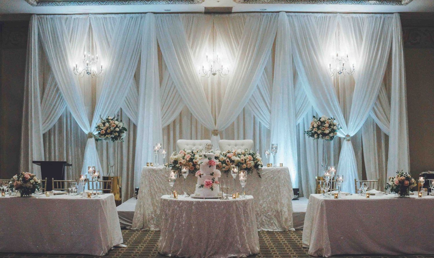 Elegant wedding reception venue with white drapes, crystal chandeliers and beautifully decorated tables.