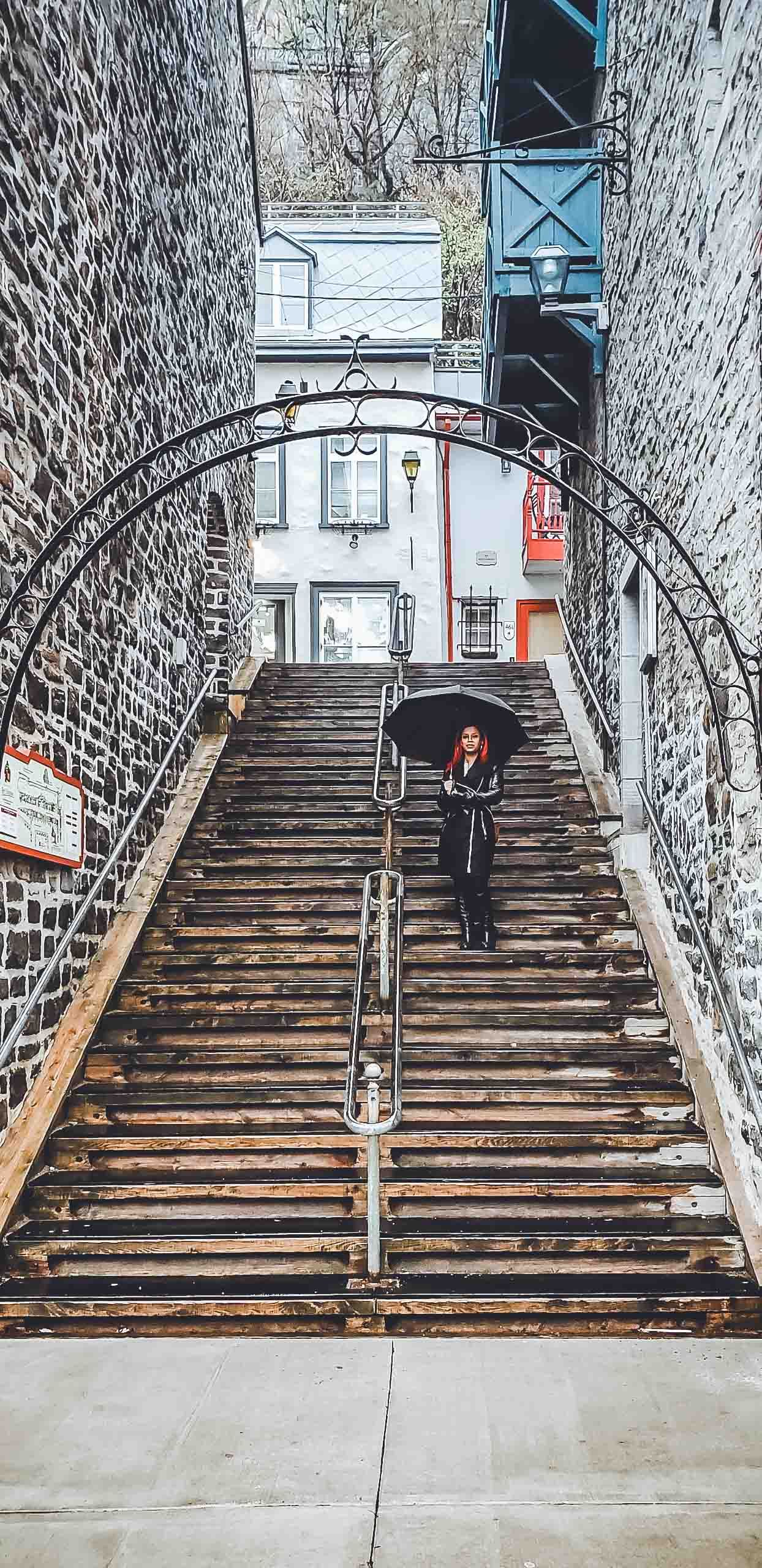 Stone staircase with metal railings and arched entrance leading up between historic buildings.