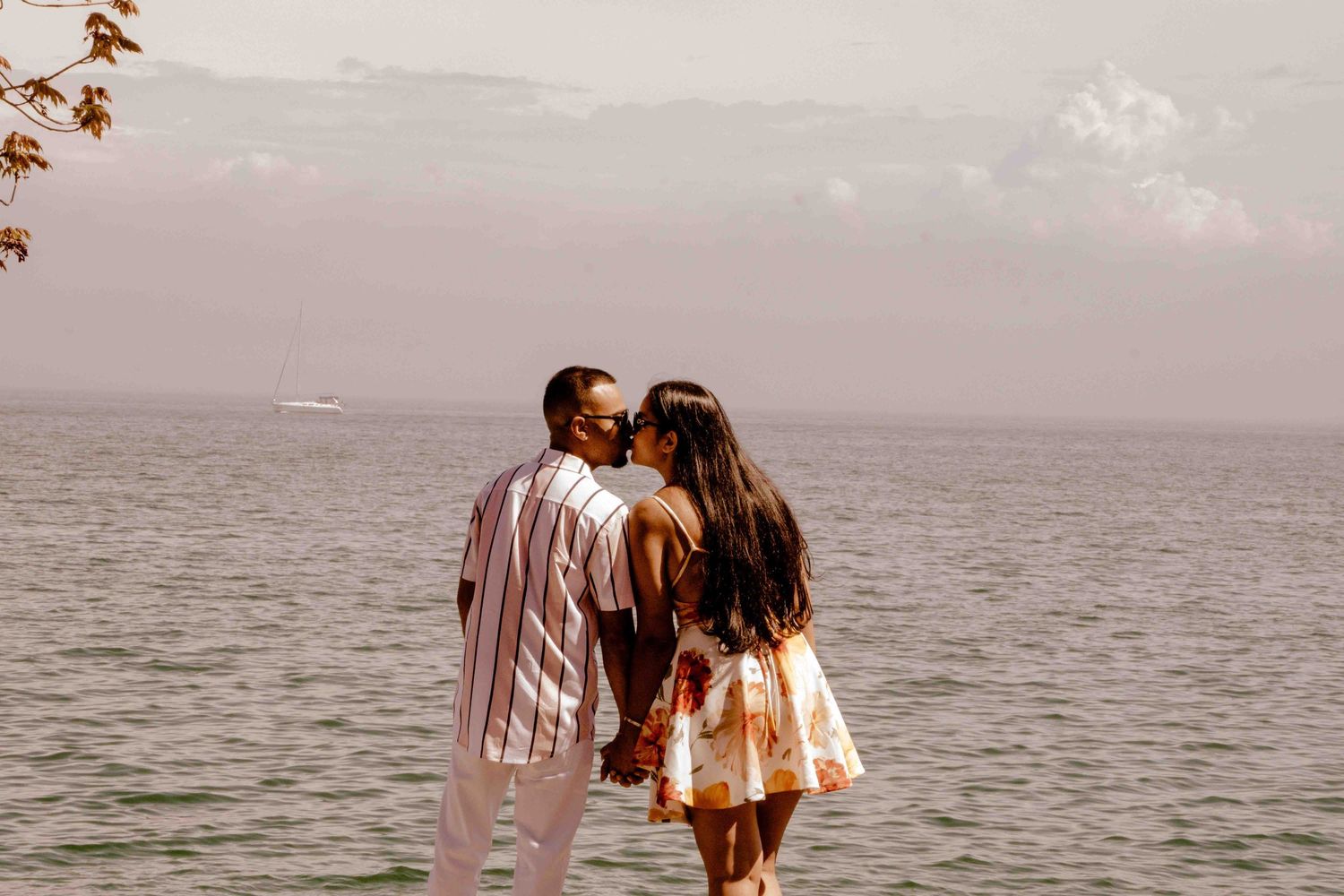 A couple in coordinated outfits embraces against an ocean backdrop during golden hour.
