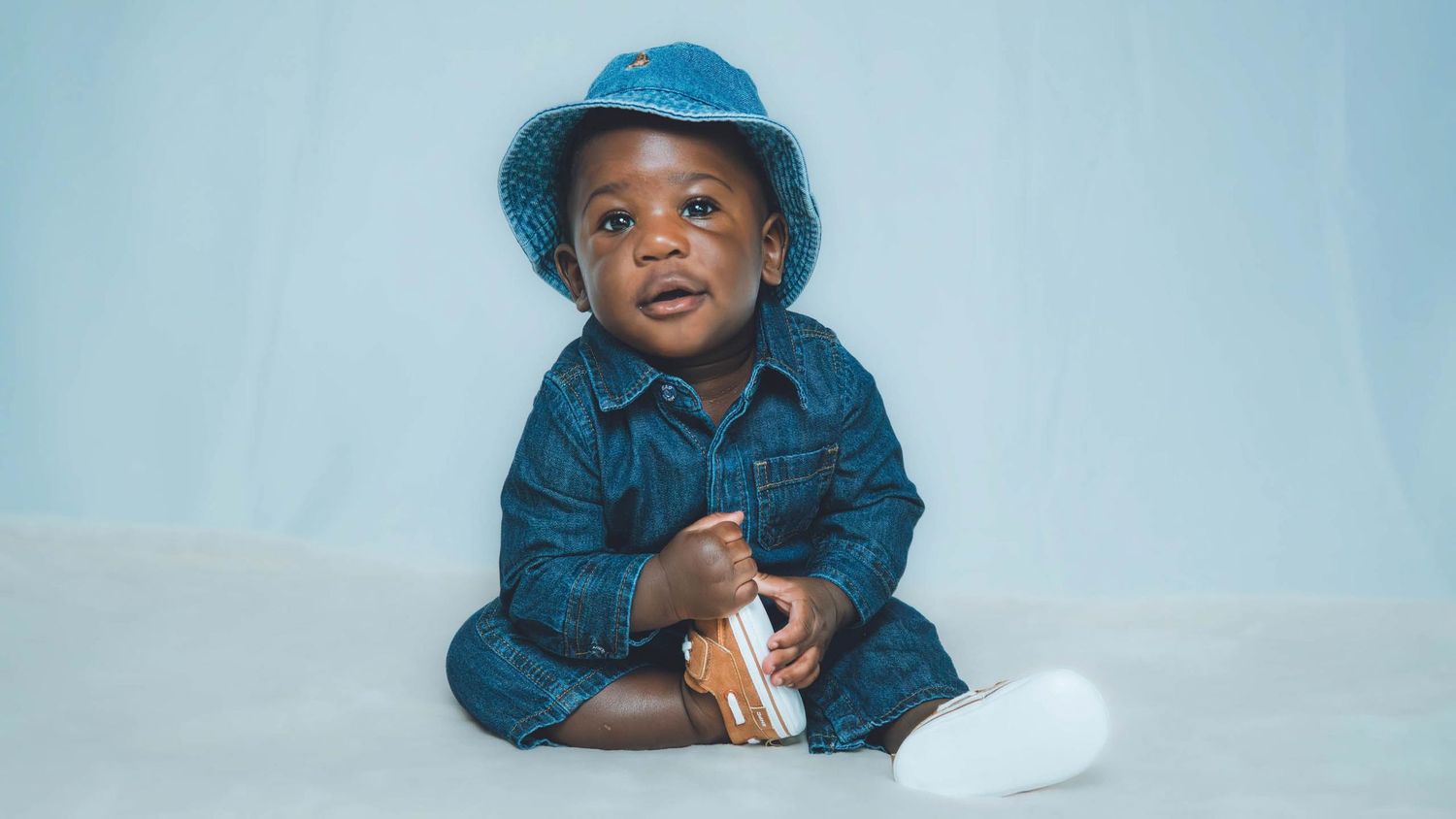 Joyful poses wearing denim and a blue bucket hat against a pale backdrop.