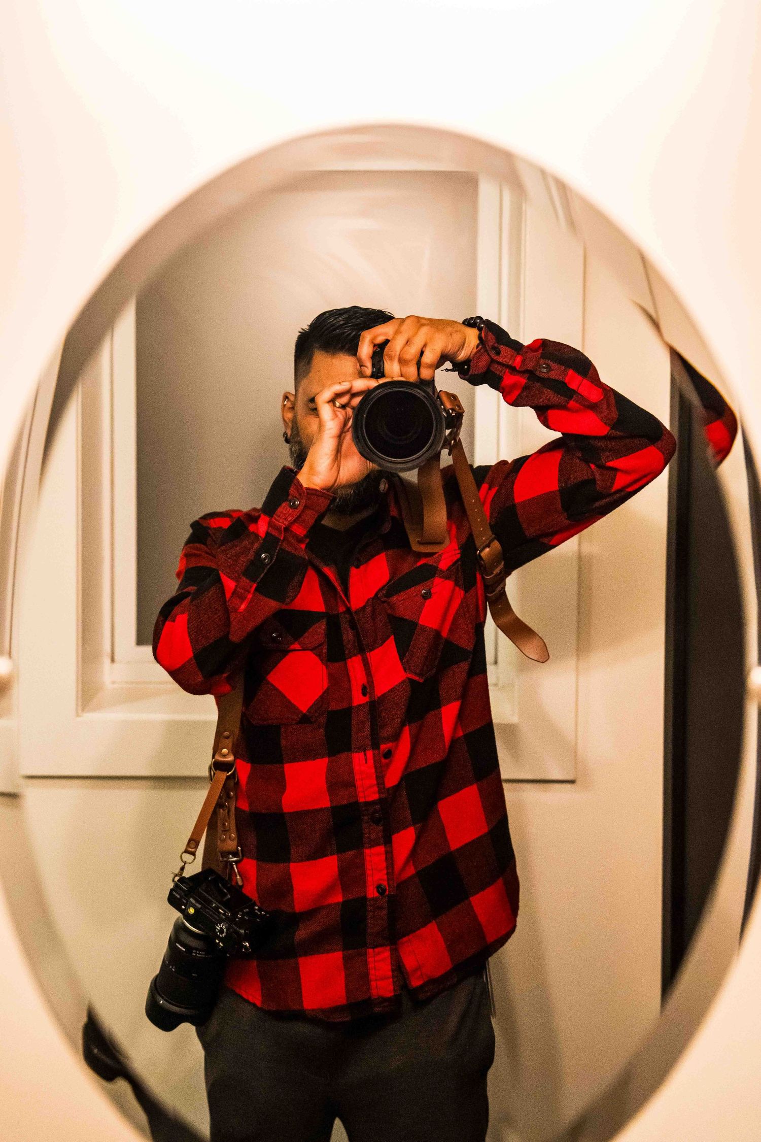 Person in red plaid flannel shirt taking mirror selfies in an oval-framed mirror.