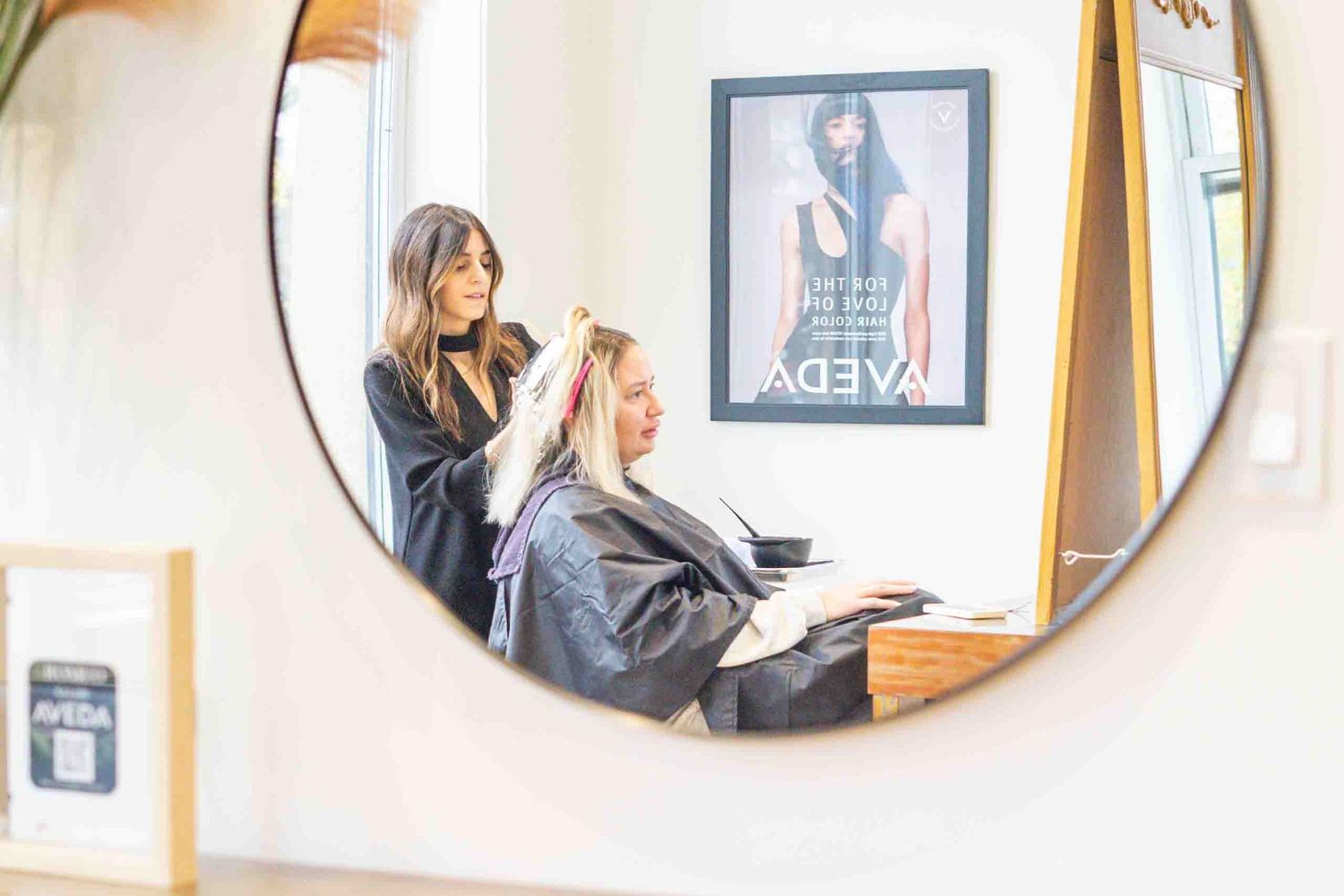 A mirror reflection shows a hair styling session in progress at a modern salon.
