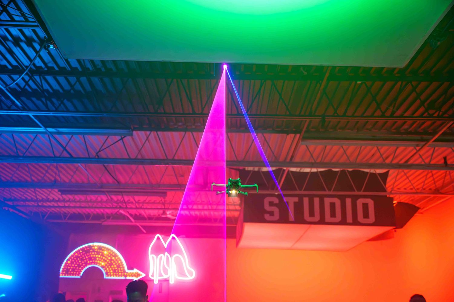 Neon lights and laser beams create a colorful display in a studio space with green and pink hues.