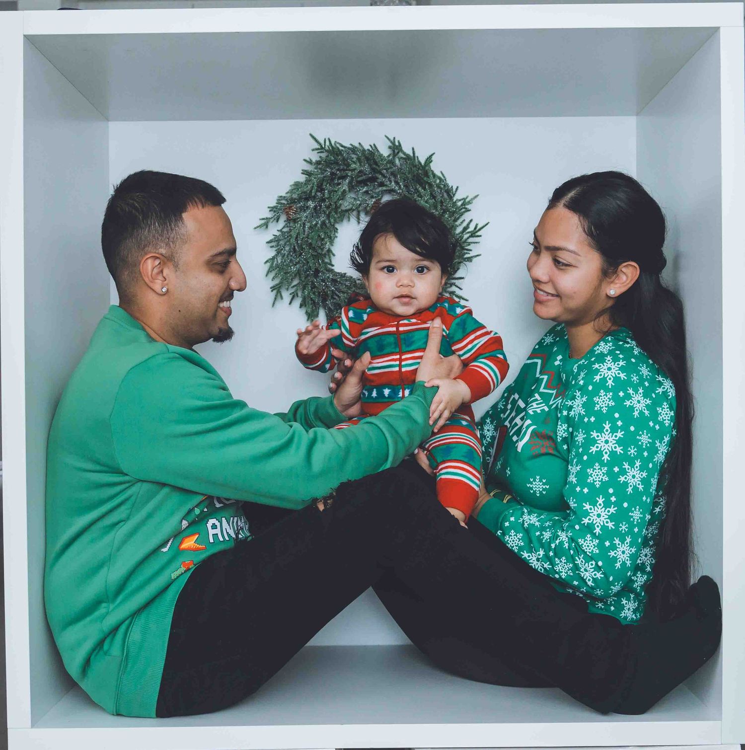 Family wearing matching green holiday sweaters posing in a white studio setting.