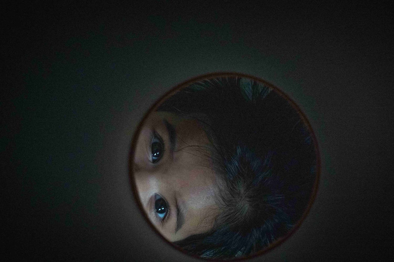 Artistic reflection of eyes in a circular mirror with dark moody lighting.