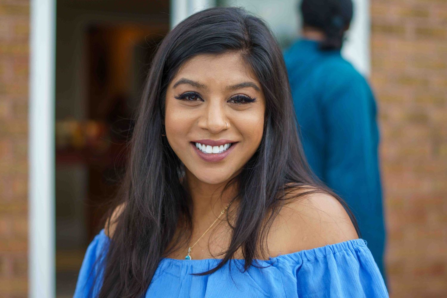 A woman in a blue off-shoulder top smiles warmly at the camera.
