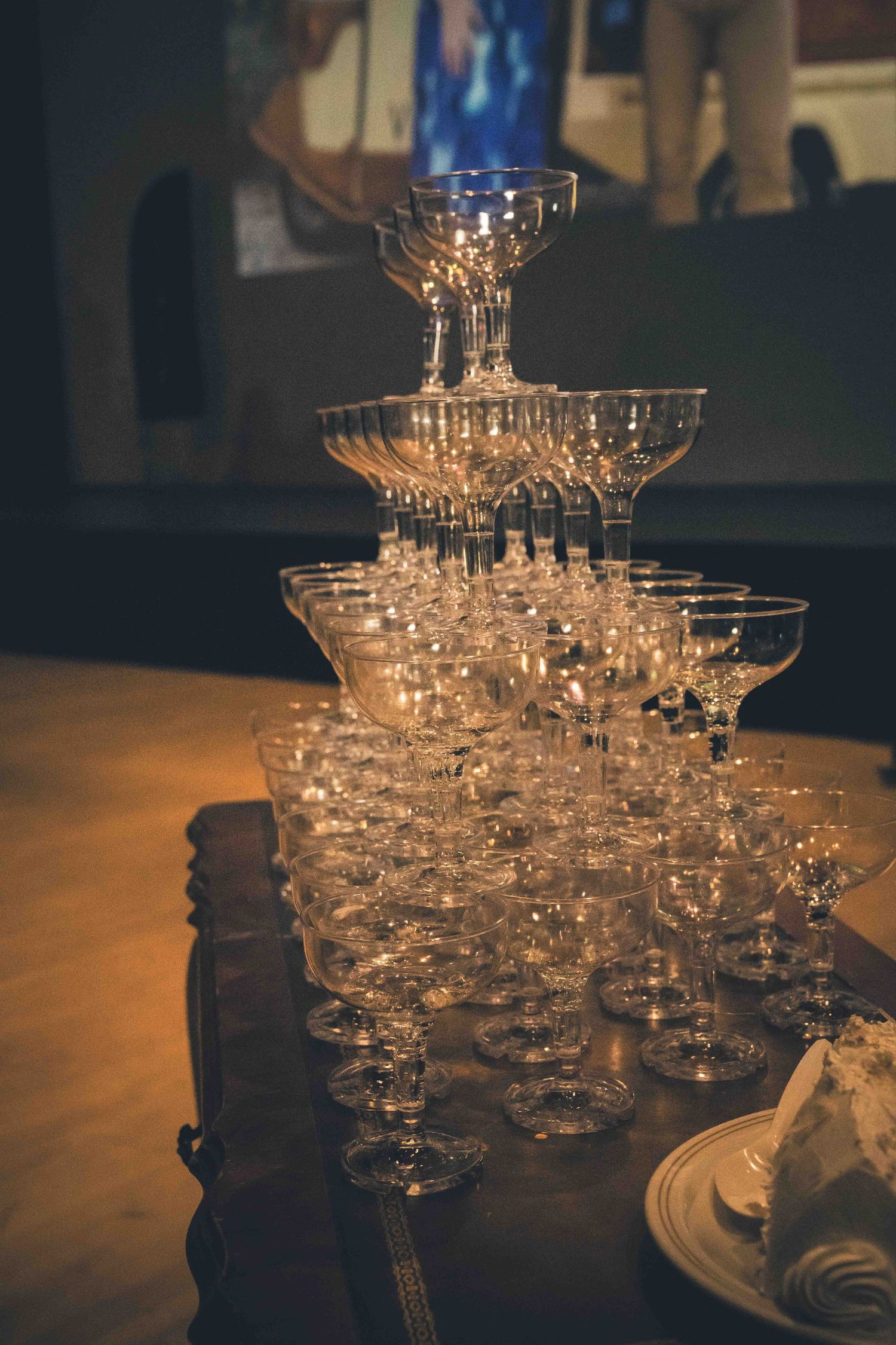 Tower of stacked champagne glasses creating an elegant fountain display on dark wooden table.