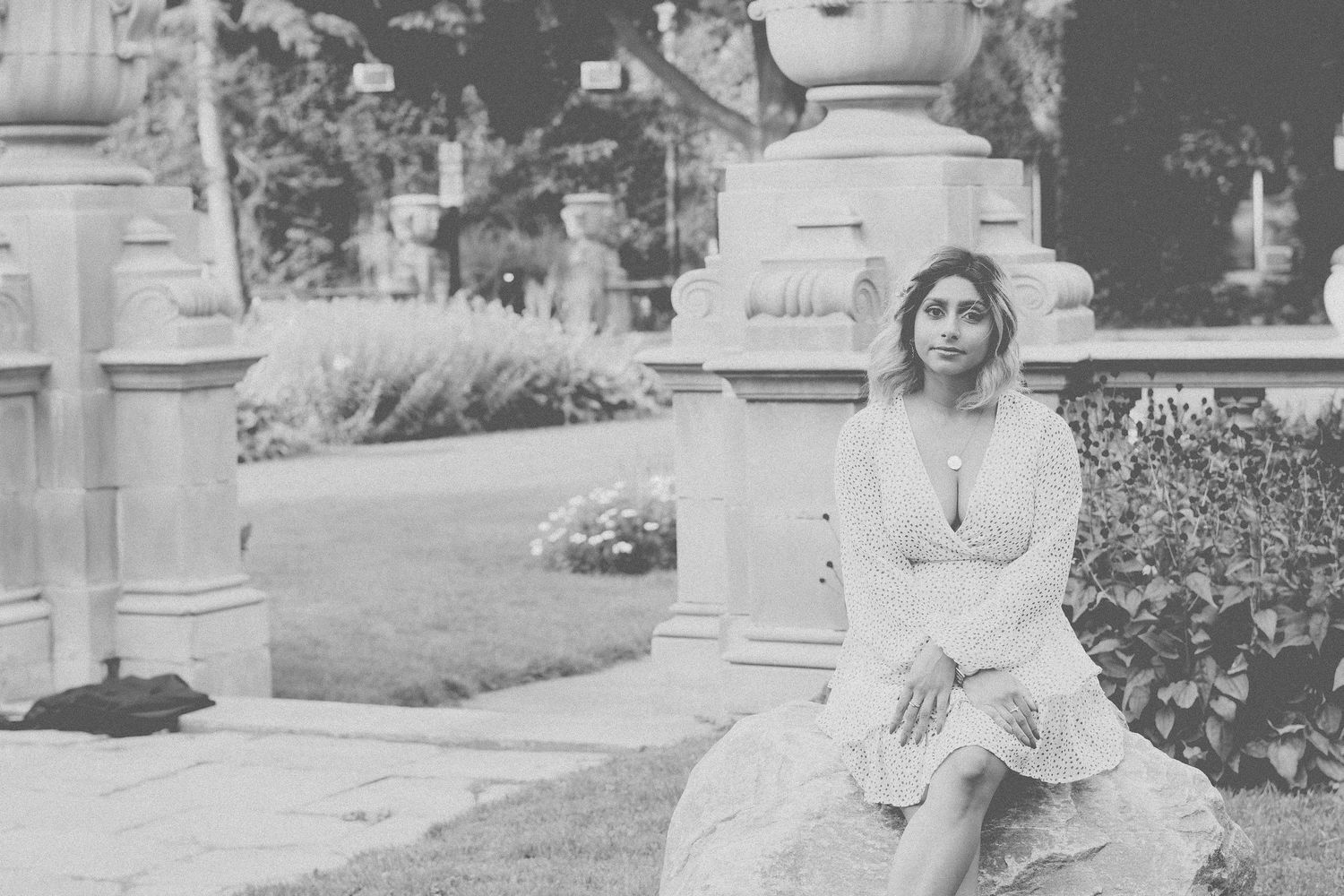 Vintage style photo of someone in a white dress sitting by stone pillars in a garden.