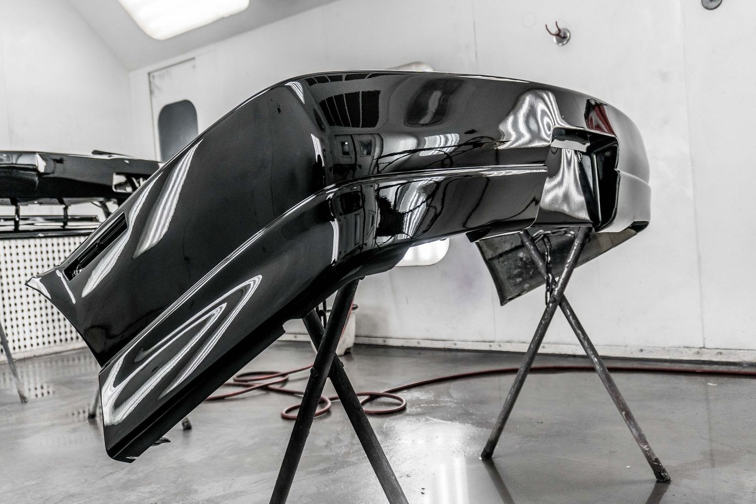 Glossy black car bumper mounted on a stand in an auto body repair shop.