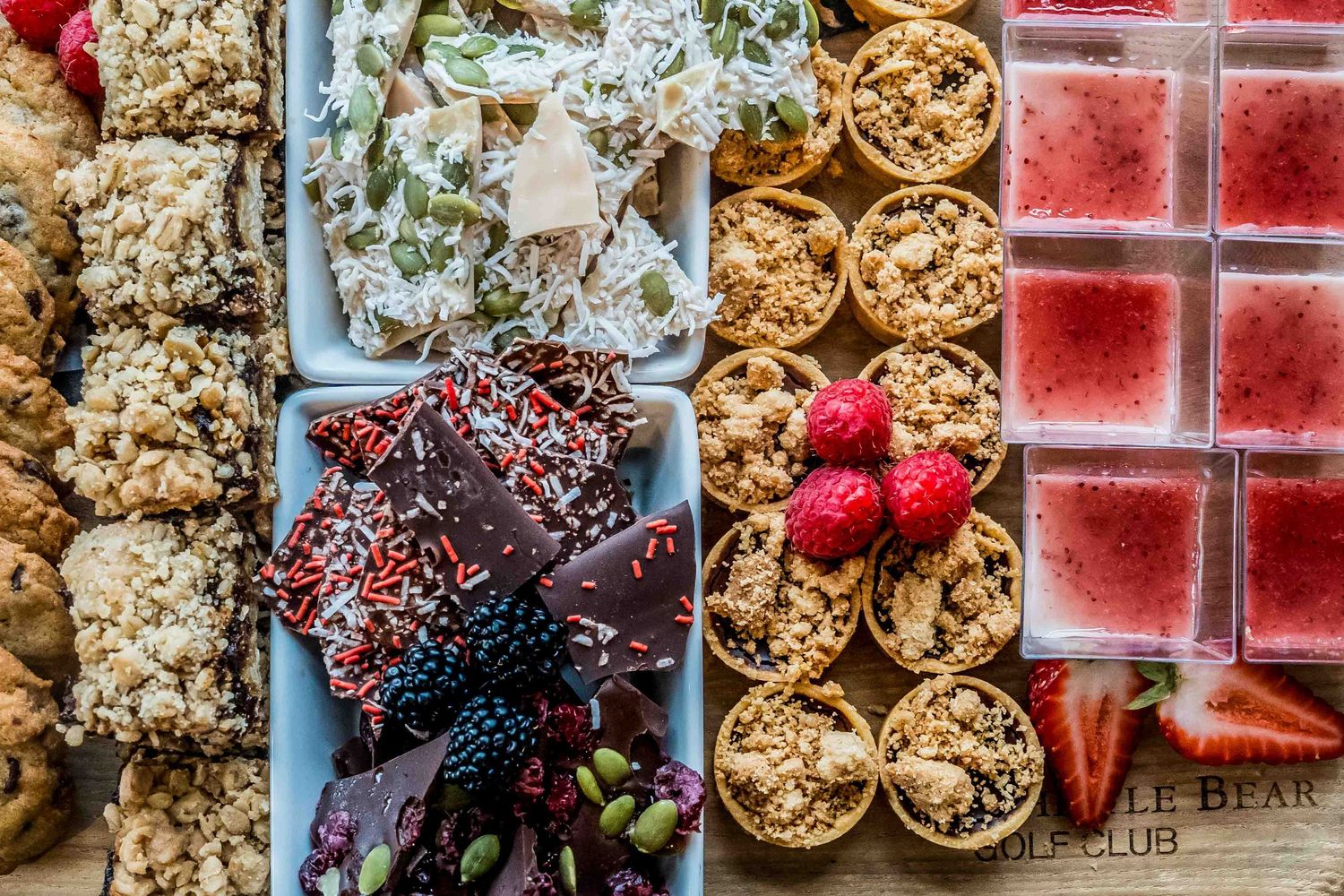 Overhead view of a gourmet dessert grazing board with cookies, chocolate, crackers, raspberries, and pink gelatin squares.