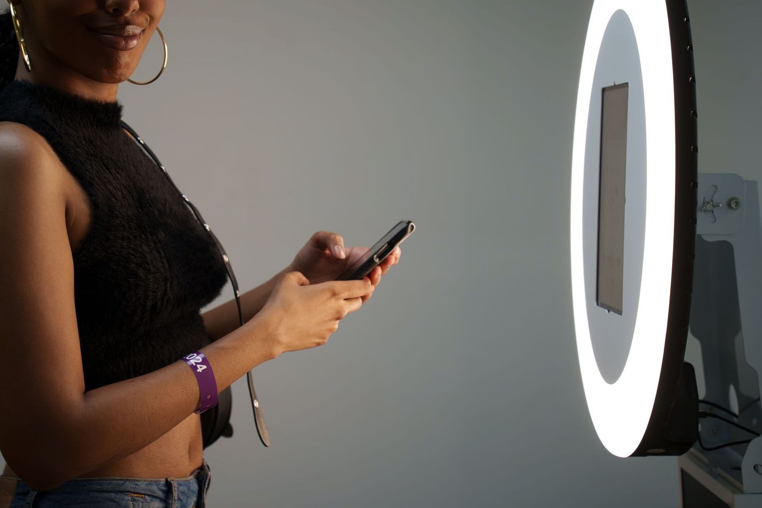 Person holding a mobile device in front of a circular ring light in a dark room.