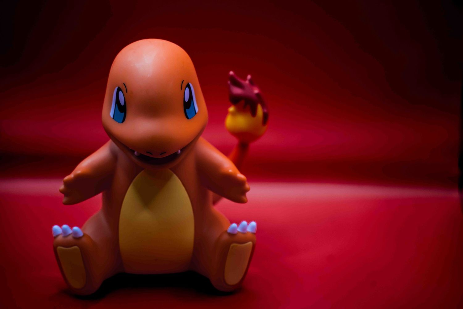 Charmander Pokemon toy figure sitting on a red background with a small flame on its tail.