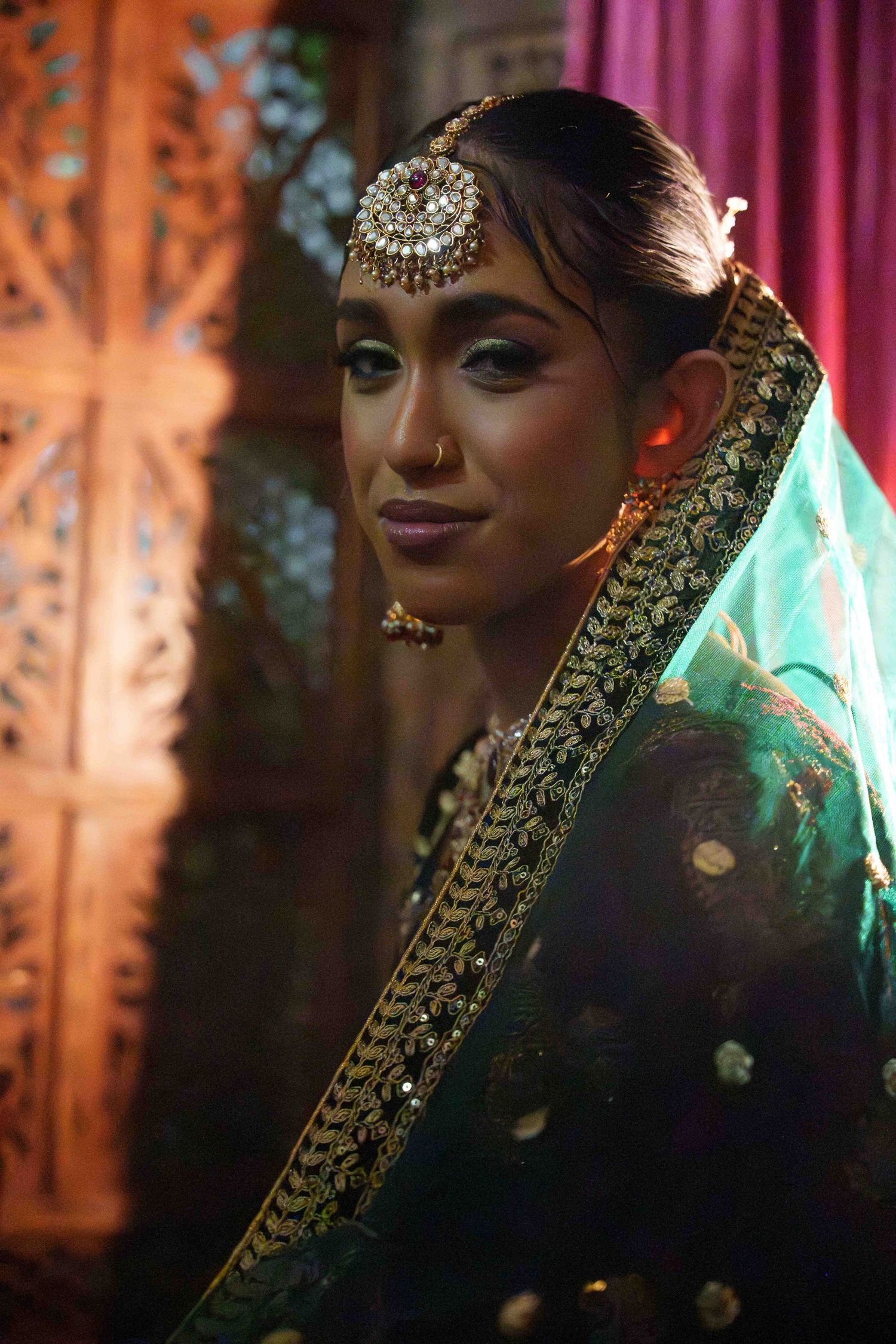 Traditional South Asian bridal portrait showing ornate jewelry and embroidered sari in rich jewel tones.