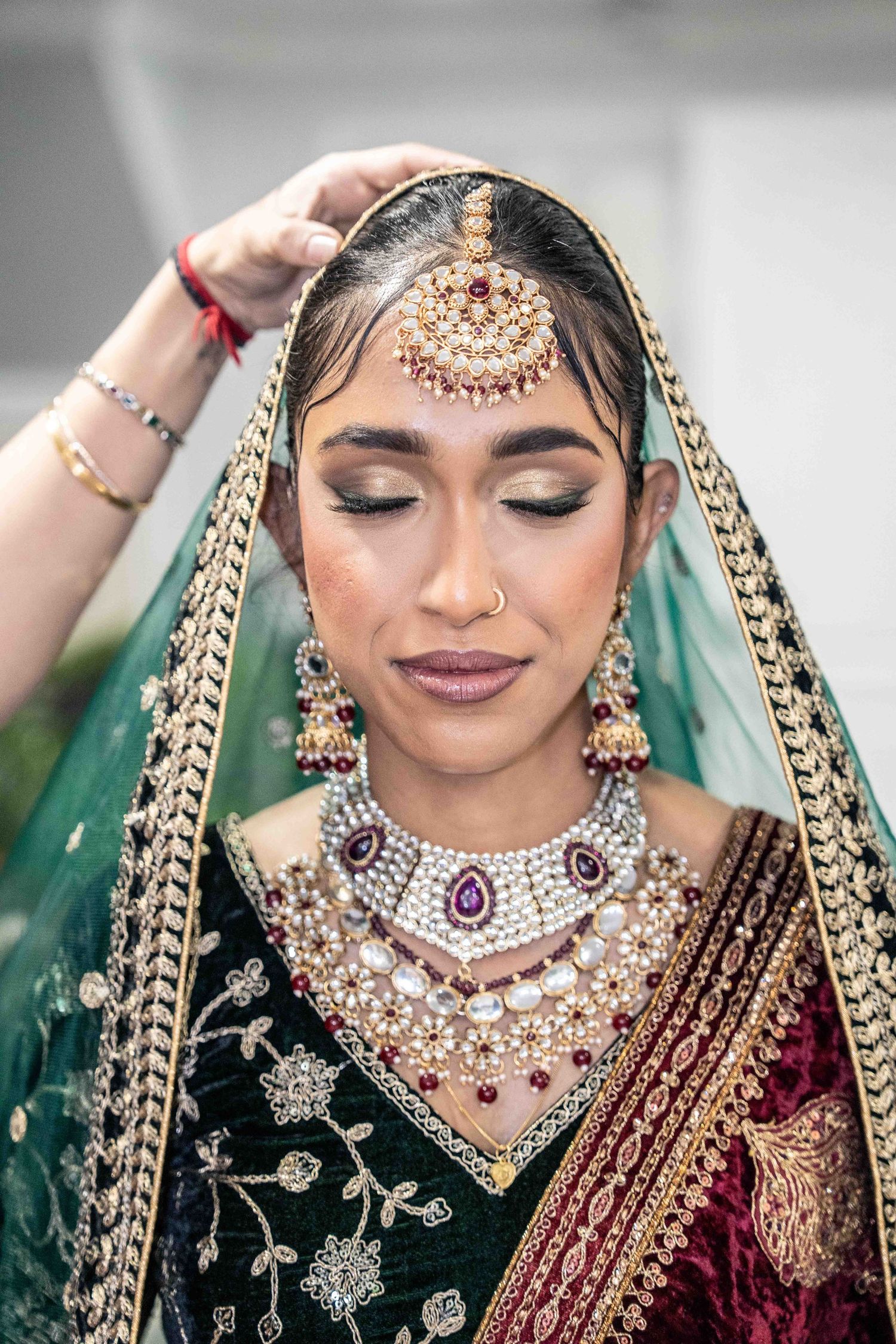 Traditional South Asian bridal attire featuring emerald green dupatta, ornate jewelry and intricate maang tikka headpiece.