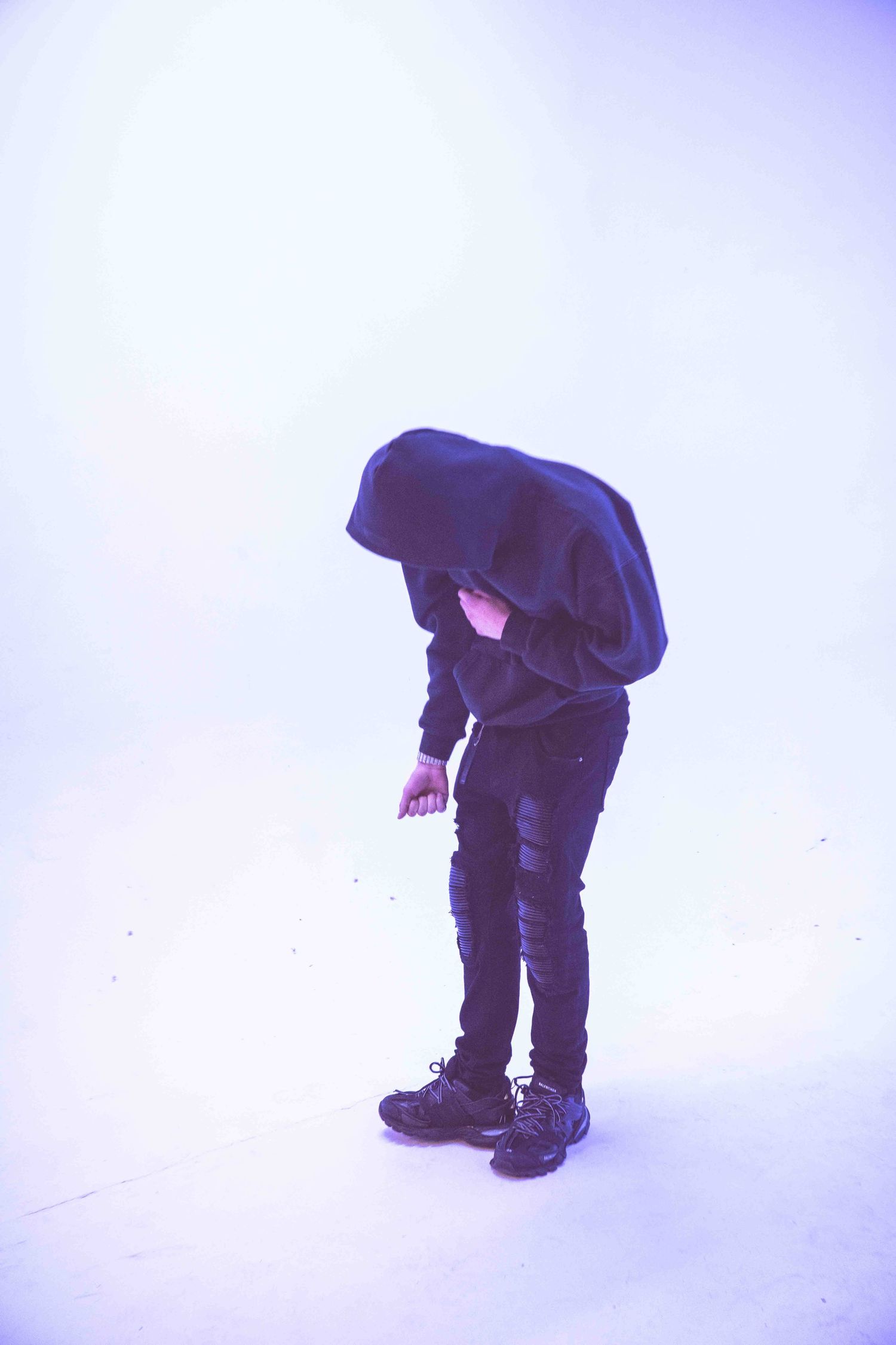Artistic silhouette of figure in dark clothing bending forward against purple-tinted background.