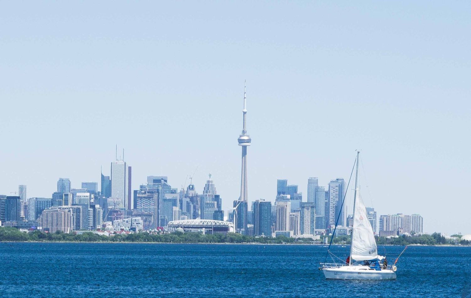 Toronto skyline view from Lake Ontario with sailboats in the foreground on a sunny day.