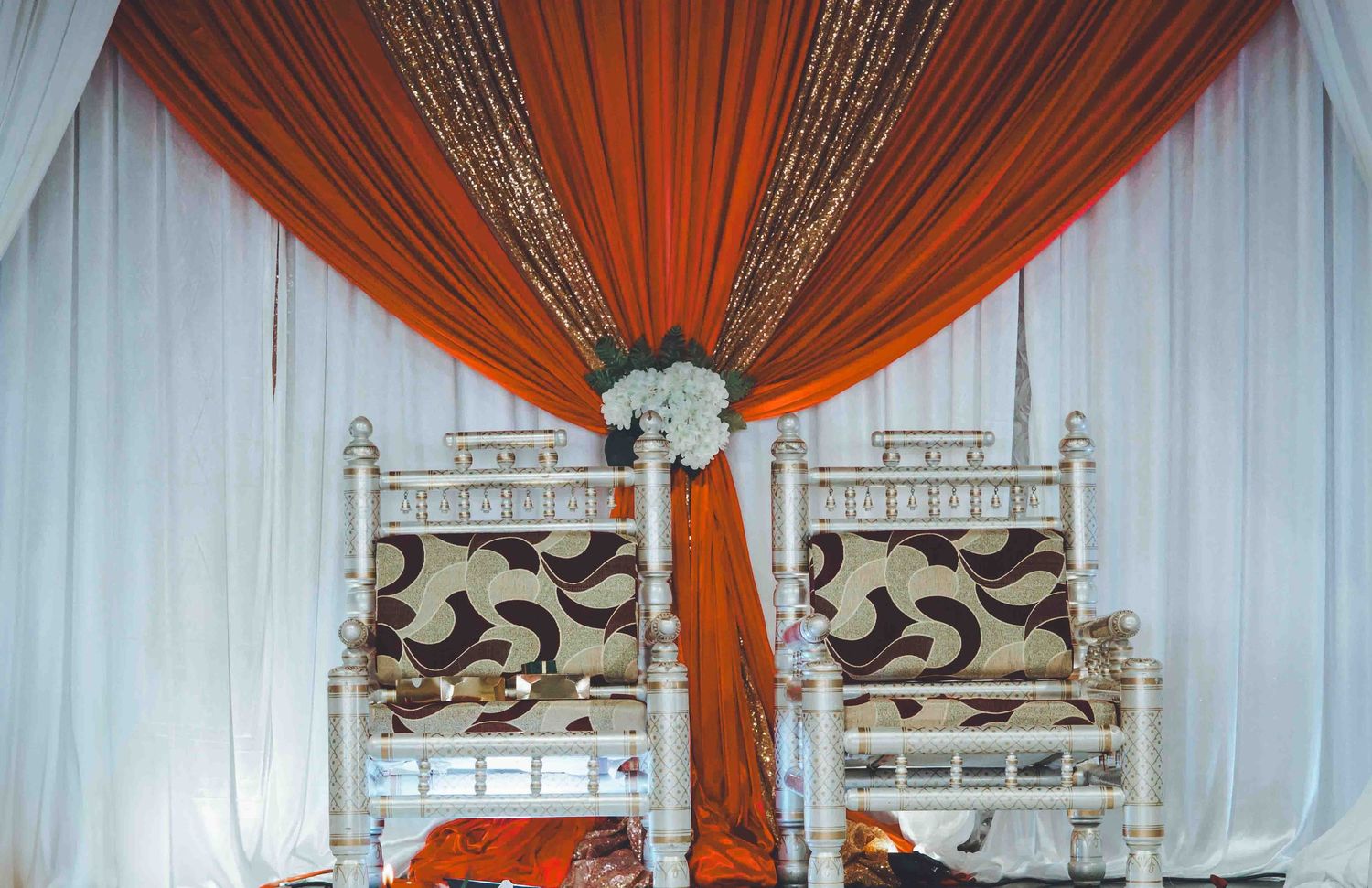Orange and white draped fabric backdrop with ornate throne chairs for a luxury event setting.