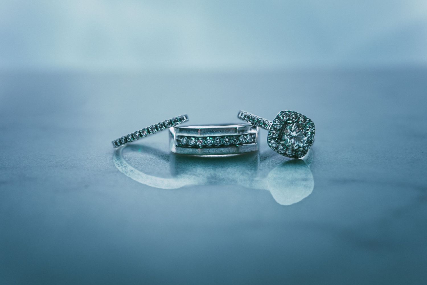 Close-up shots of engagement rings and wedding bands against a dreamy blue background.