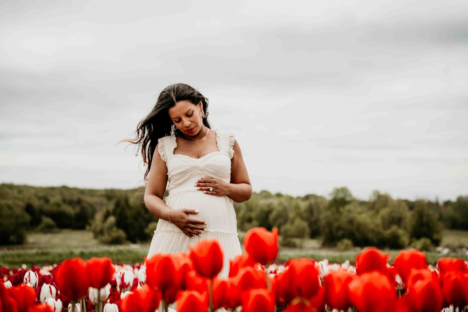 Dramatic black and white maternity portrait among blooming red tulips in a field.