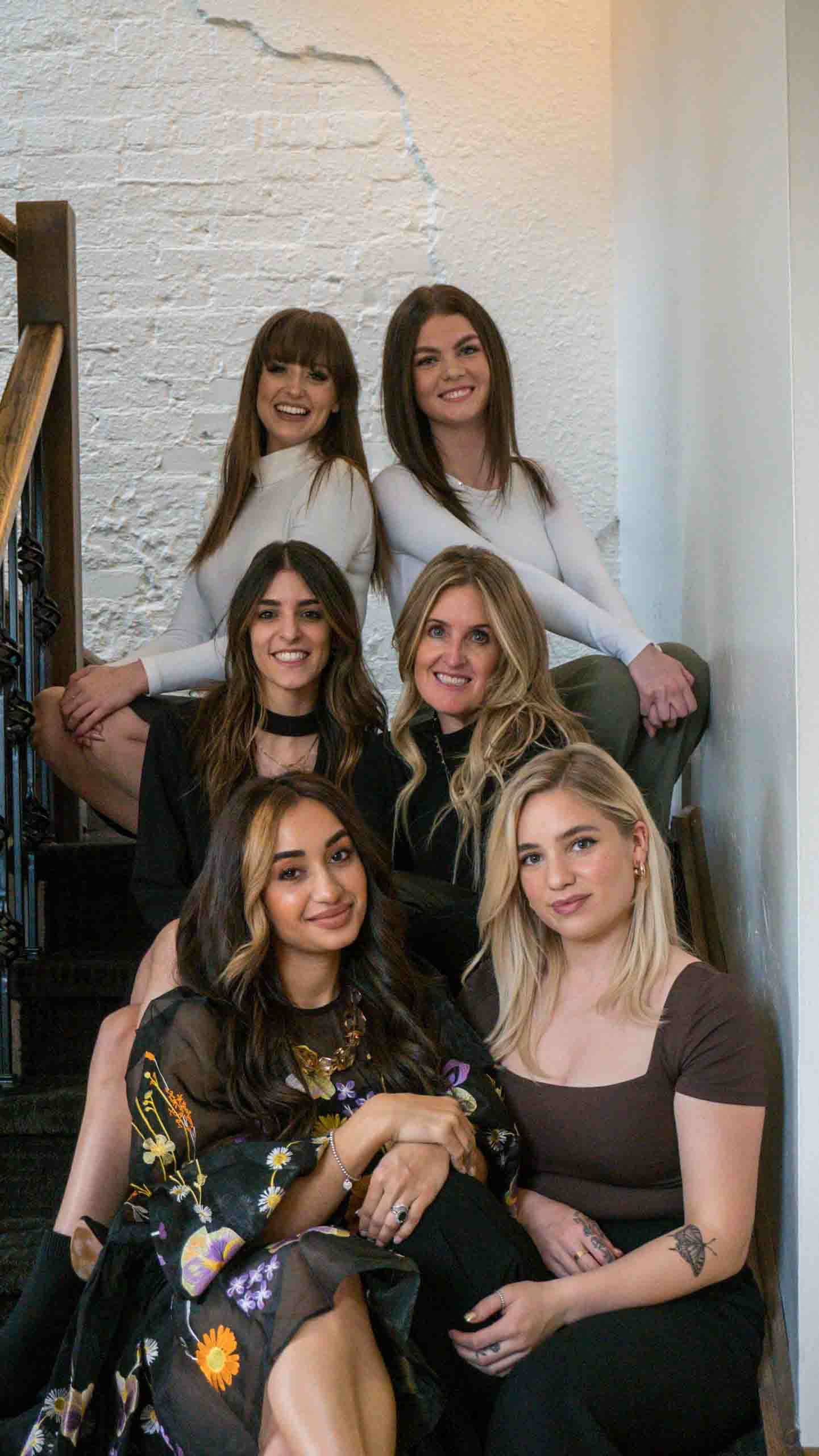 Salon staff gathered for a casual group photo in front of white brick wall.