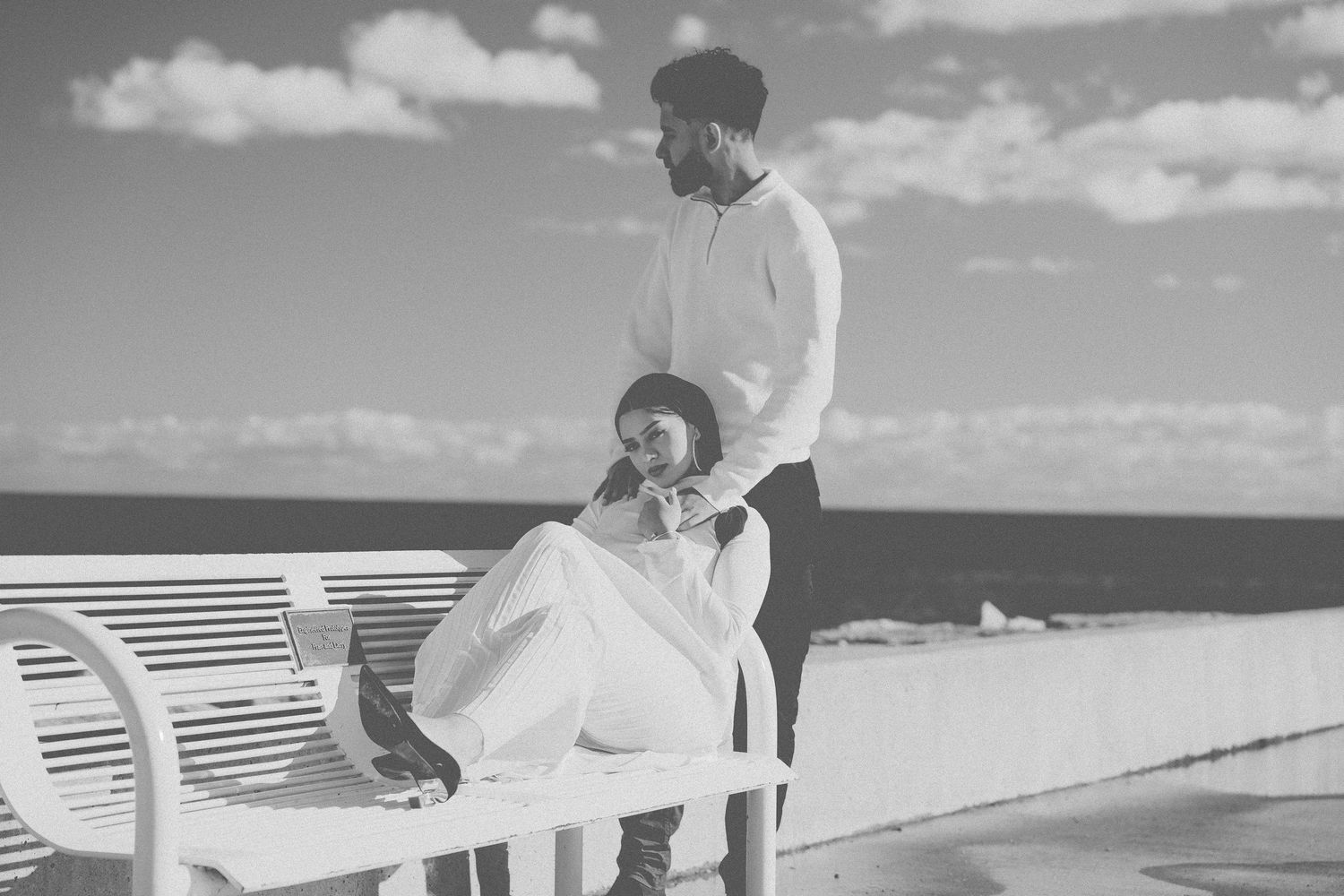 Couple sitting on rocks by waterfront on sunny day with blue sky.