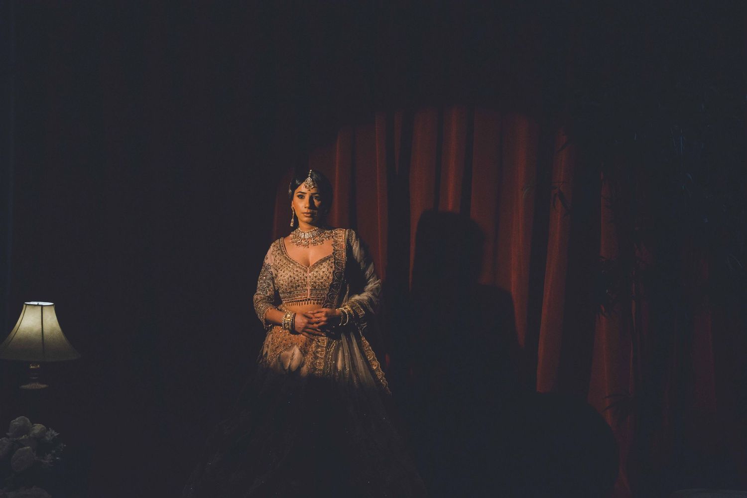 Dark moody stage performance with dramatic red curtain and vintage lamp lighting.