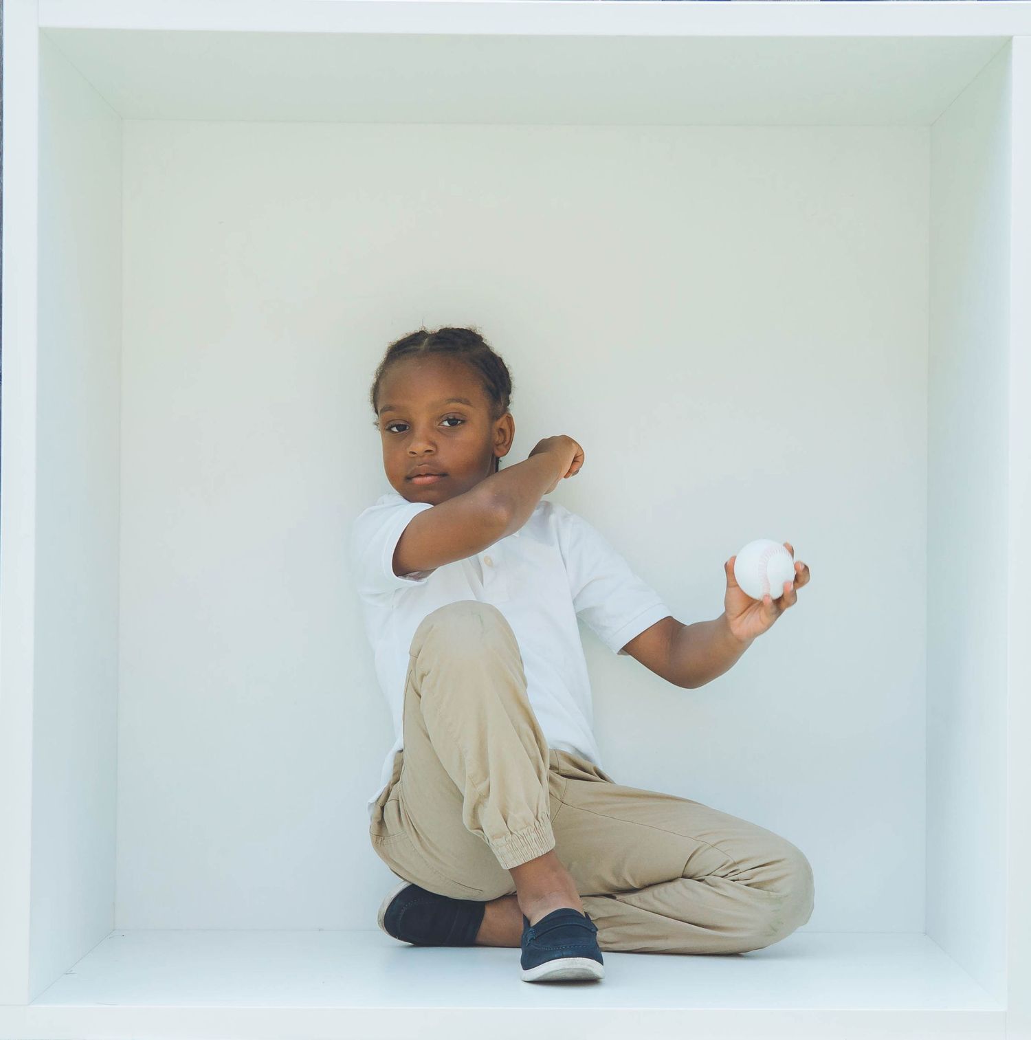 Child posing playfully with a football in a minimalist white studio space.