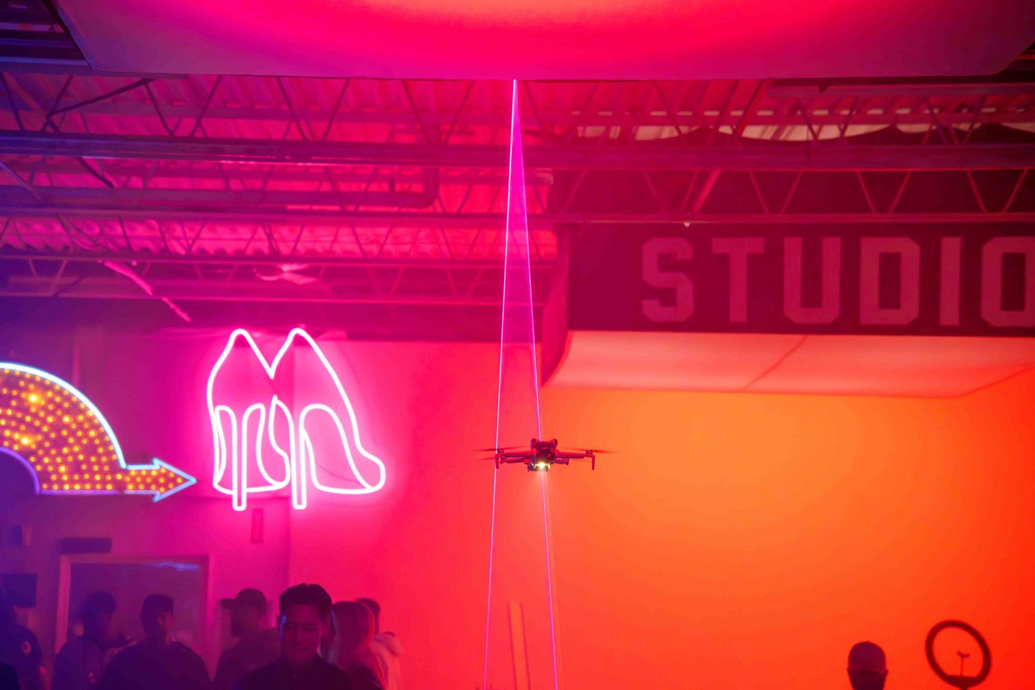 A drone performs in a studio with vibrant pink lighting and neon signs.
