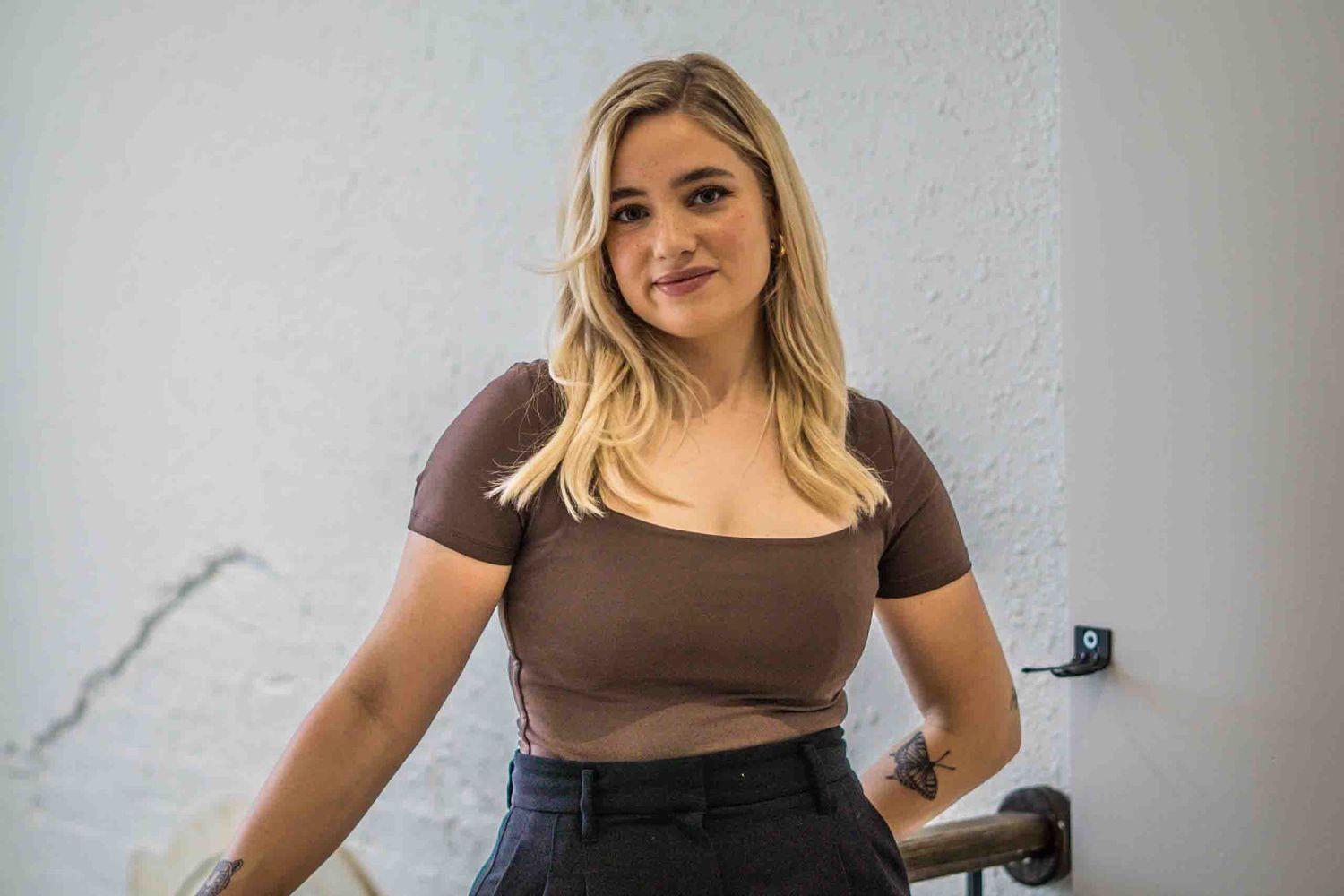 A casual salon look featuring a brown crop top and high-waisted jeans against a white wall.