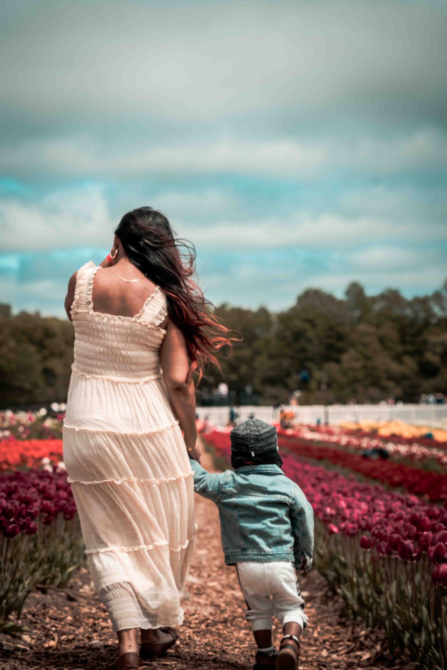 Person in flowing white dress walking with small child through flower fields.