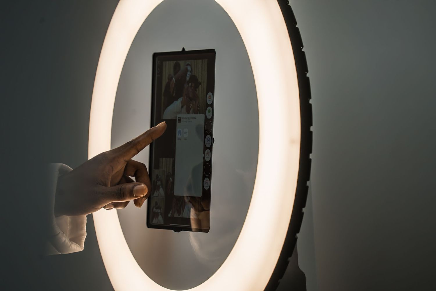 Hand pointing at a screen mounted within a large circular LED light fixture.