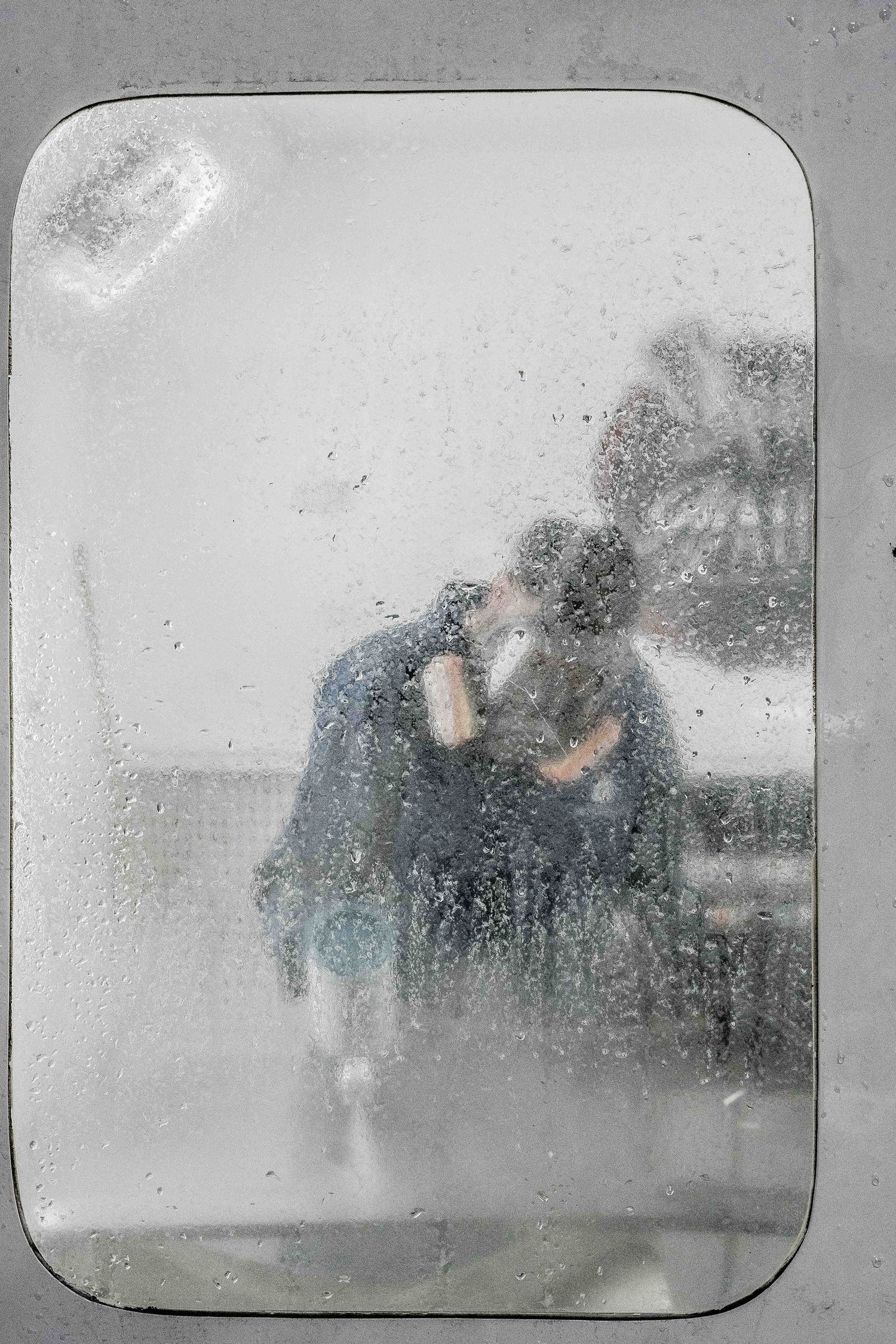 Raindrops on a window create a blurry view of figures in the distance on a foggy day.