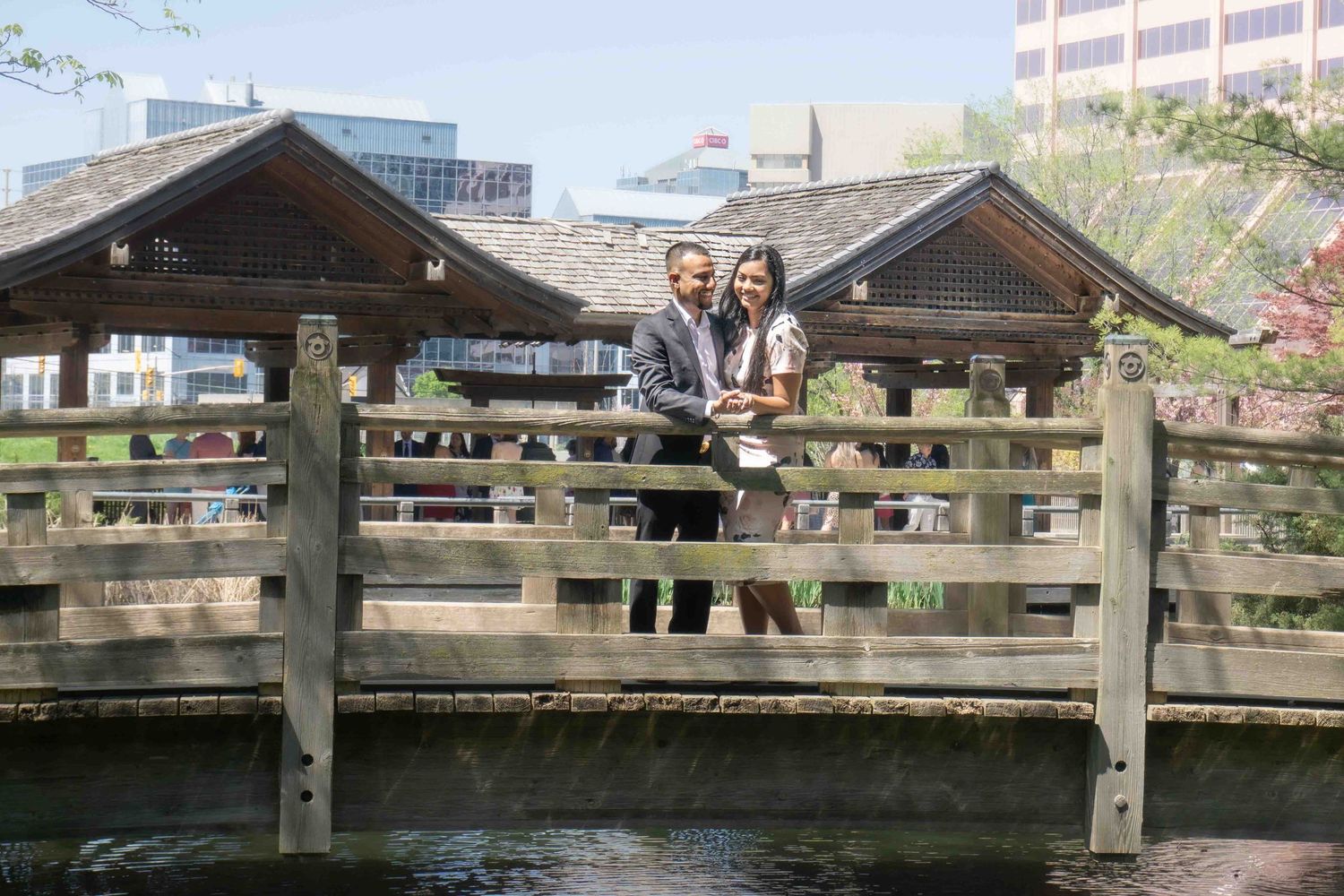 Students gather on a wooden bridge in a park-like setting during graduation celebrations.