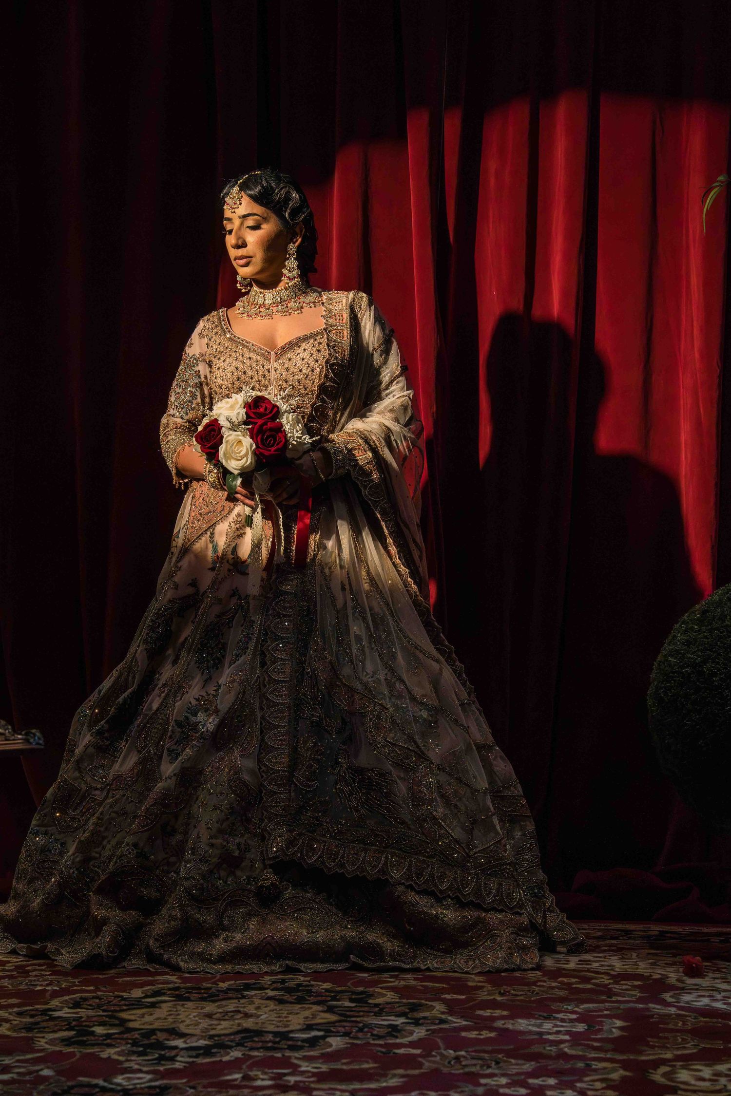 A performer in an elaborate Victorian-style gown with lace and ruffles poses dramatically against red curtains on stage.