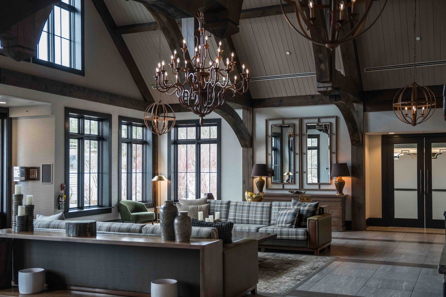 Rustic luxury hotel lobby with vaulted ceilings, elegant chandeliers, and plush seating areas bathed in natural light.