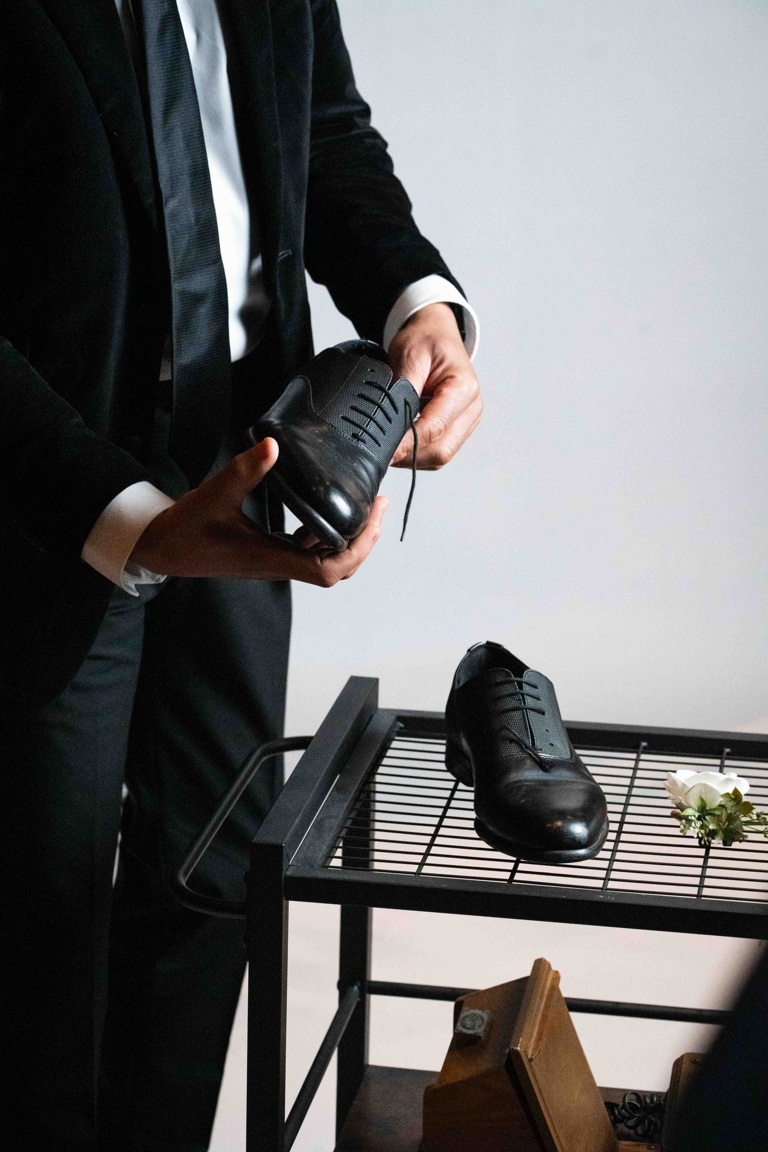 Professional in a black suit adjusts their sleeve cuff while standing near a window with horizontal blinds.