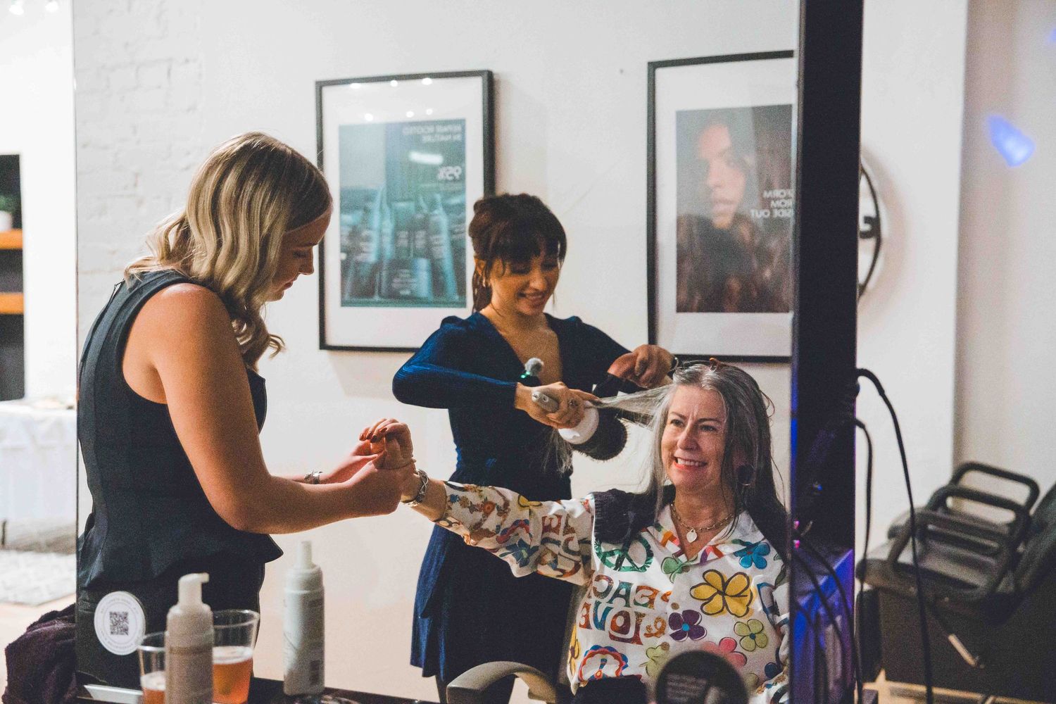 Three women laughing and interacting at an indoor social event or salon.