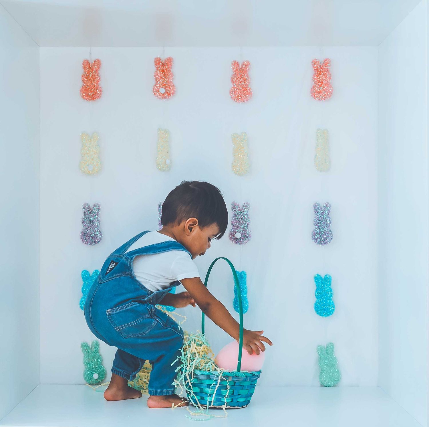 Child in blue outfit interacting with colorful bunny decorations on white wall.