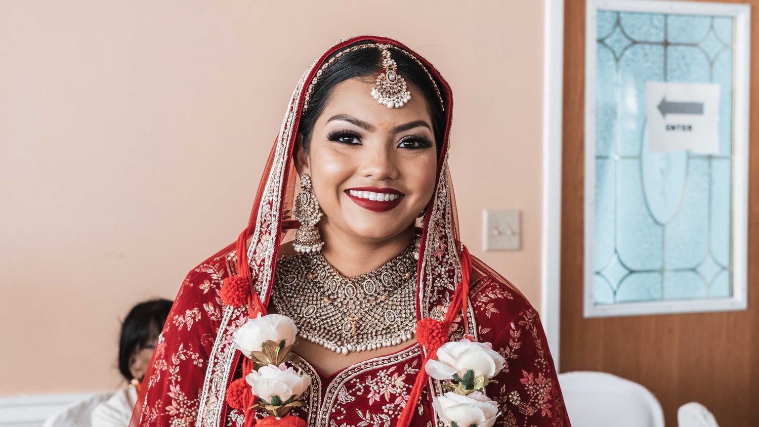 Traditional South Asian bride wearing an ornate red and gold wedding outfit with intricate jewelry and accessories.