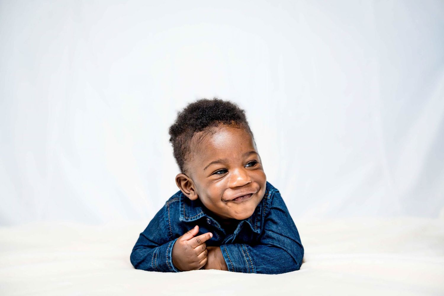 Child wearing blue denim jacket poses with bright smile against white background.