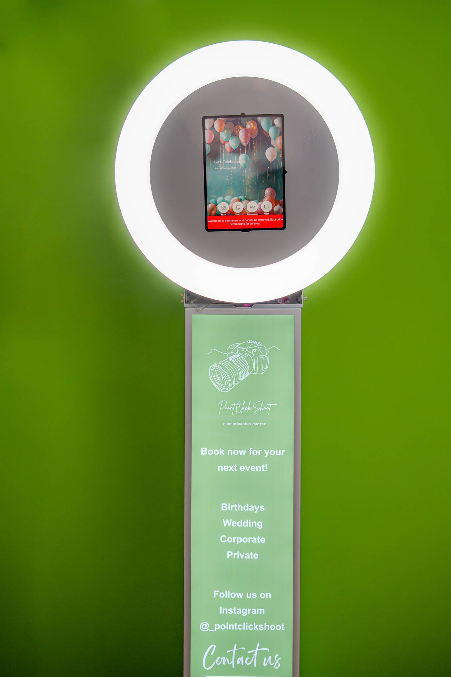 Ring light photo booth setup with green background and digital display screen.