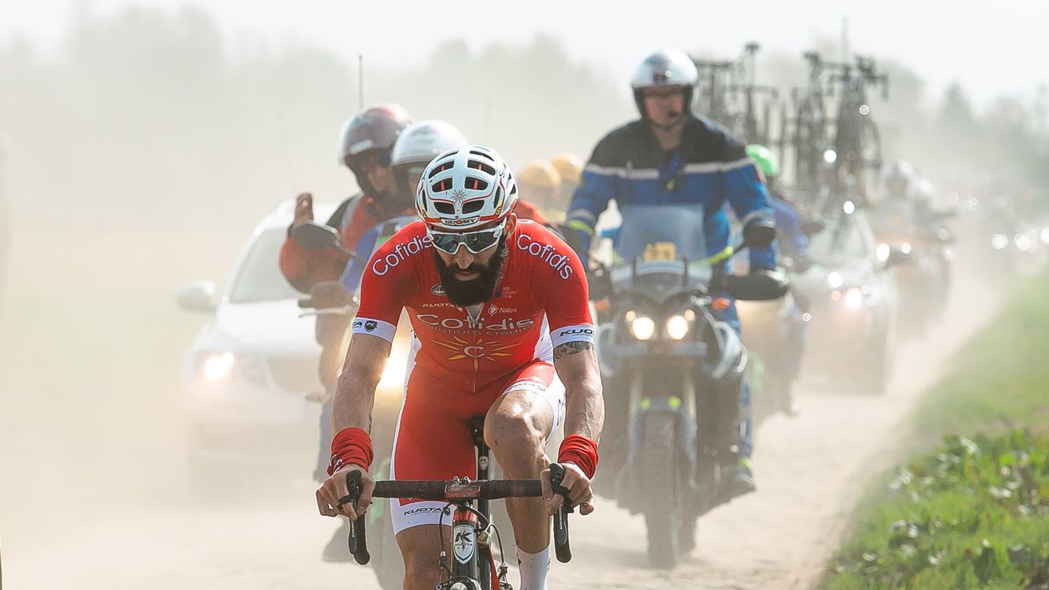 Cyclist in red jersey races through dusty gravel road during a professional cycling competition.