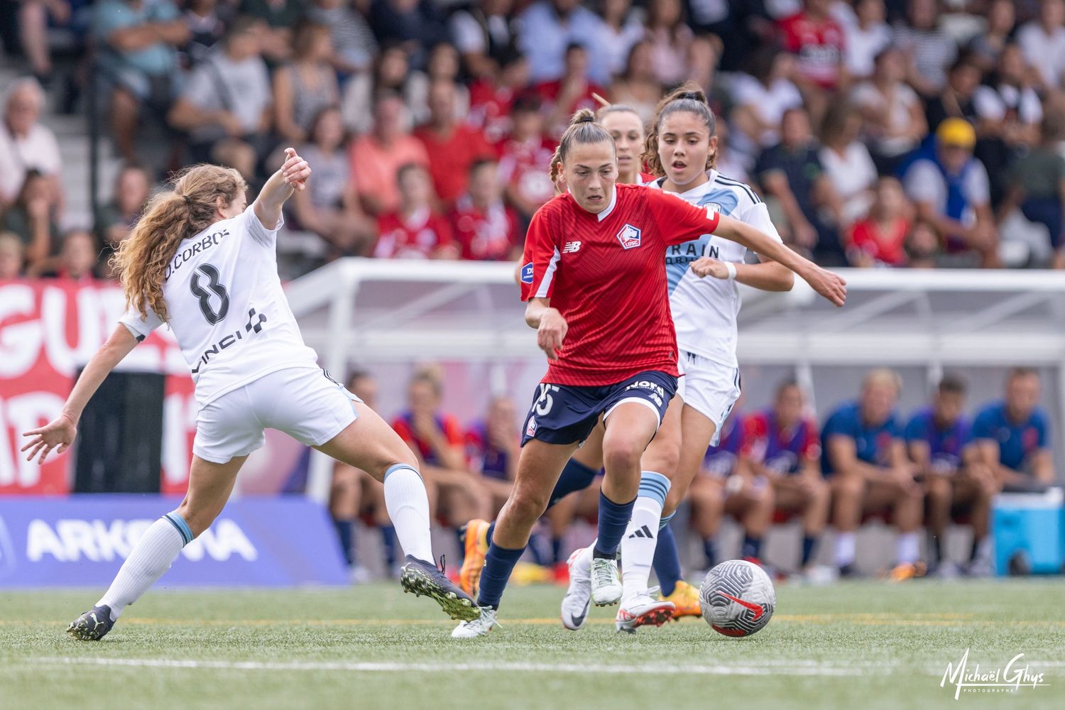 Female soccer players competing for the ball during an intense women's football match on a green grass field.