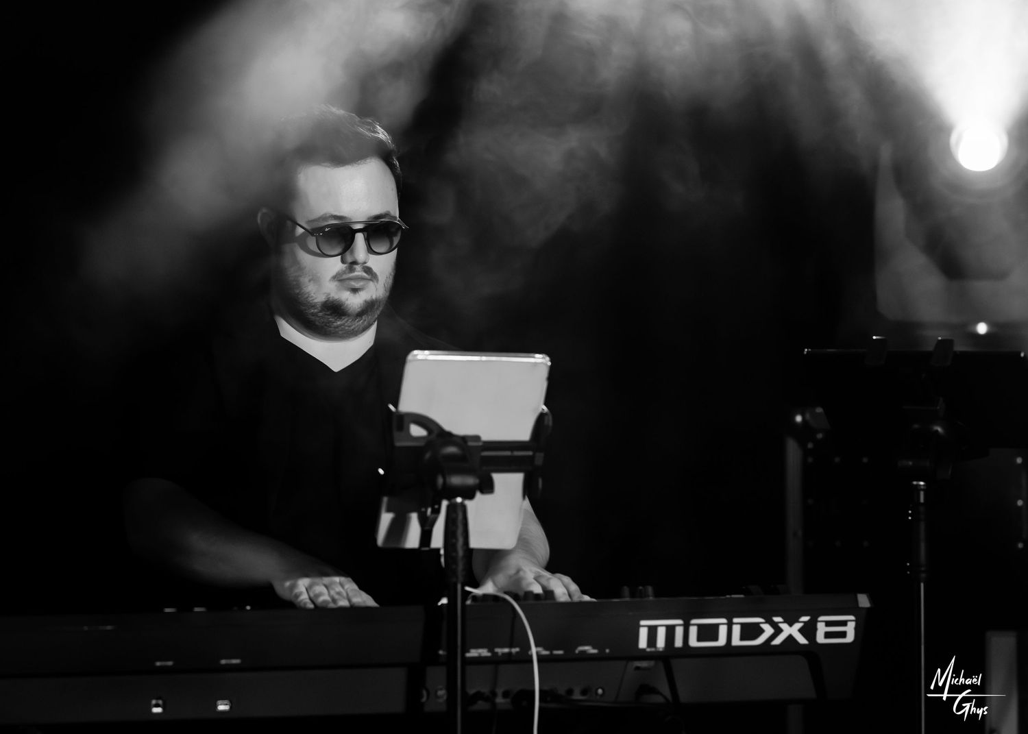 Black and white photo of a keyboard musician playing a Yamaha MODX8 synthesizer on a smoky concert stage.