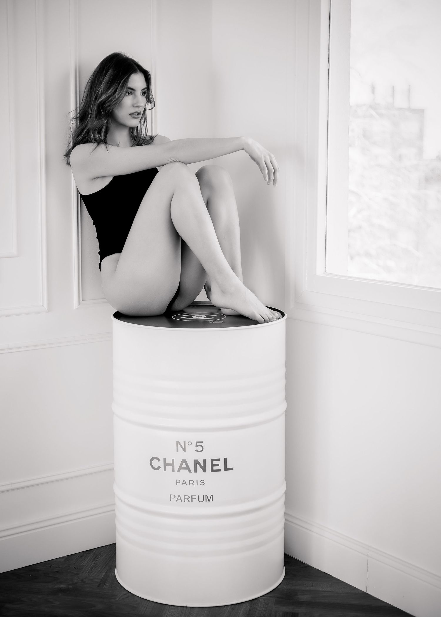 Photo de mode en noir et blanc d'une jeune femme en body assise sur un bidon Chanel No.5.- Michaël GHYS Photographe Lille